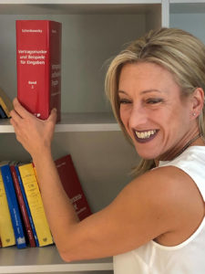 Rechtsanwältin Mag. Karin Luxbacher beim Bücherregal lachend